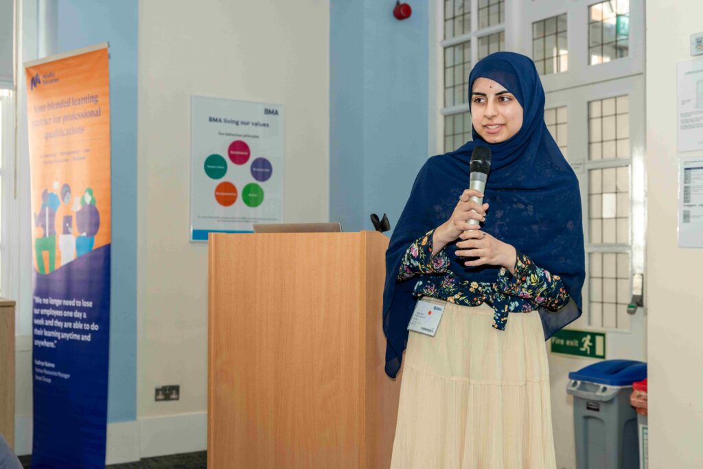 A Mindful Education apprentice holding a microphone and speaking to other Mindful Education employees about the benefits of an apprenticeship and how they provide necessary skills for work.