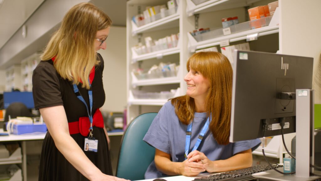 An apprentice and their employer speaking with each other whilst using a desktop.